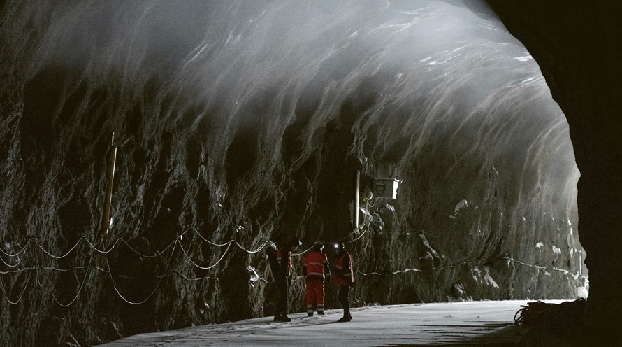 Drei Männer stehen in einem dunklen Tunnel. Auf dem Boden liegt Schnee und von rechts dringt Licht herein.