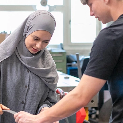 Eine junge Frau mit Kopftuch und ein junger Mann arbeiten gemeinsam an einem Gegenstand.