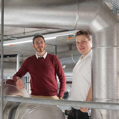 Zwei Projektverantwortliche stehen in den Produktionsanlagen des Wärmeverbund Frick, es sind grosse Leitungen zu sehen.