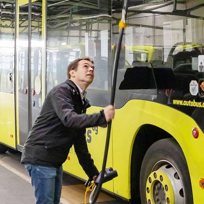 Ein Mann steht vor einem gelben Bus und hält ein Ladekabel, das an der Decke der Halle befestigt ist.