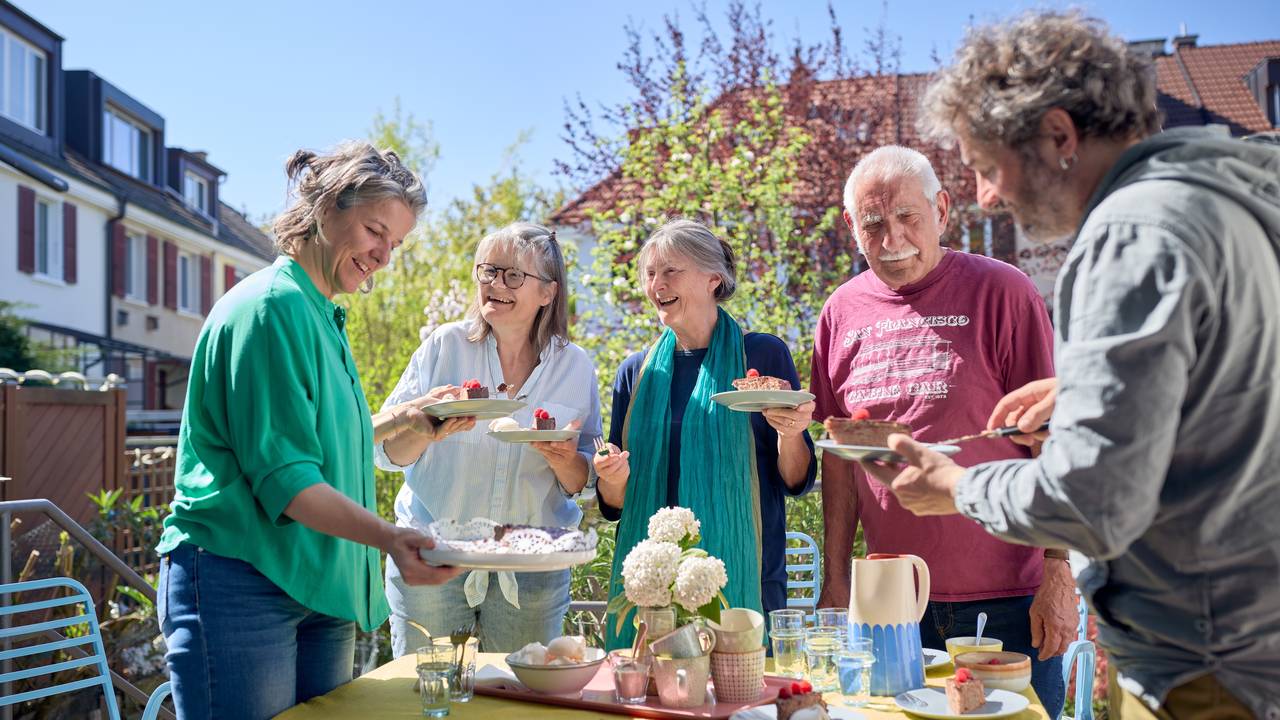 Gruppe von fünf Menschen, die in einem Gartentisch stehen und sich unterhalten. 