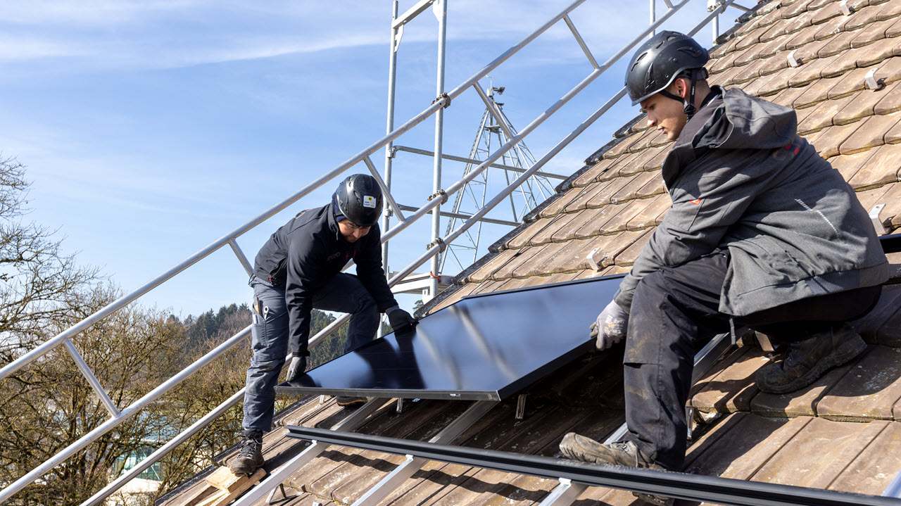 Zwei Senero-MItarbeitende montieren ein PV-Modul auf einem Dach.