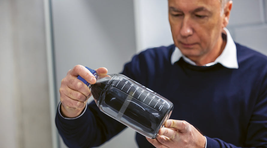 Thomas Meier hält eine Flasche hoch, die schwarze Pulveraktivkohle enthält.