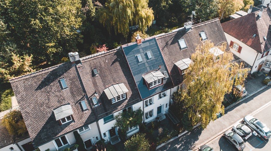 Blick aus der Vogelperspektive auf eine Reihe Einfamilienhäuser. Das Mittlere hat eine Solaranlage im Dach integriert.