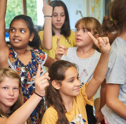 Schülerinnen einer Primarschulklasse strecken den Finger.