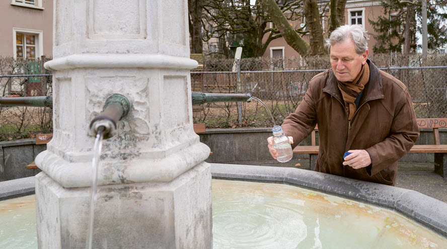 Philipp Hübner lehnt sich an einen Brunnentrog und füllt eine Flasche mit Wasser.