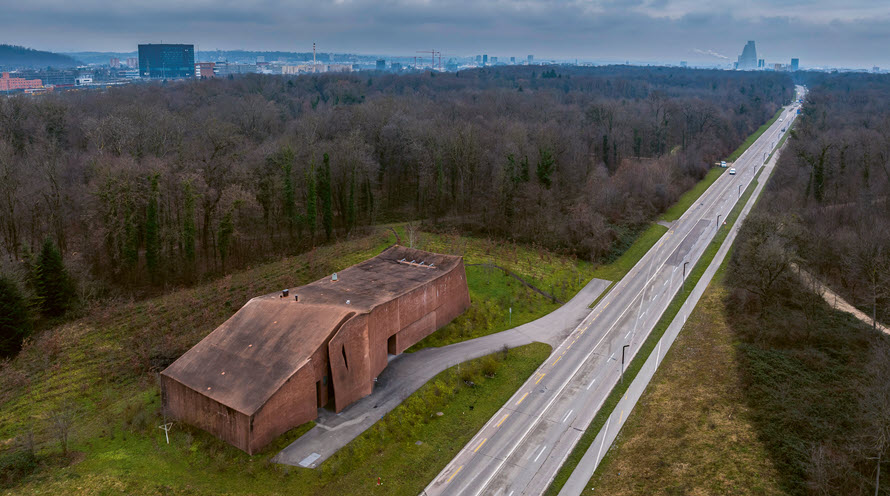 Luftaufnahme mit Blick auf die Trinkwasseraufbereitungsanlage. Drum herum ist Wald und am Horizont die Stadt Basel.