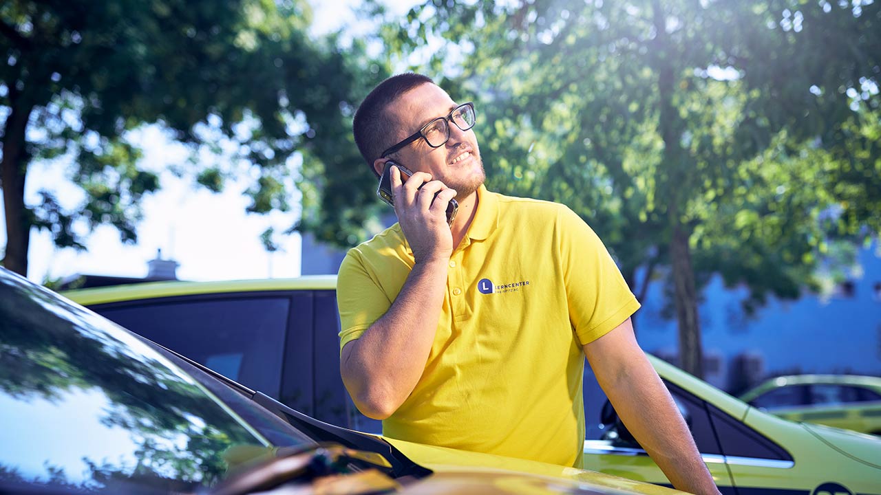 Ein Mann telefoniert neben einem Auto und schaut dabei nach oben.