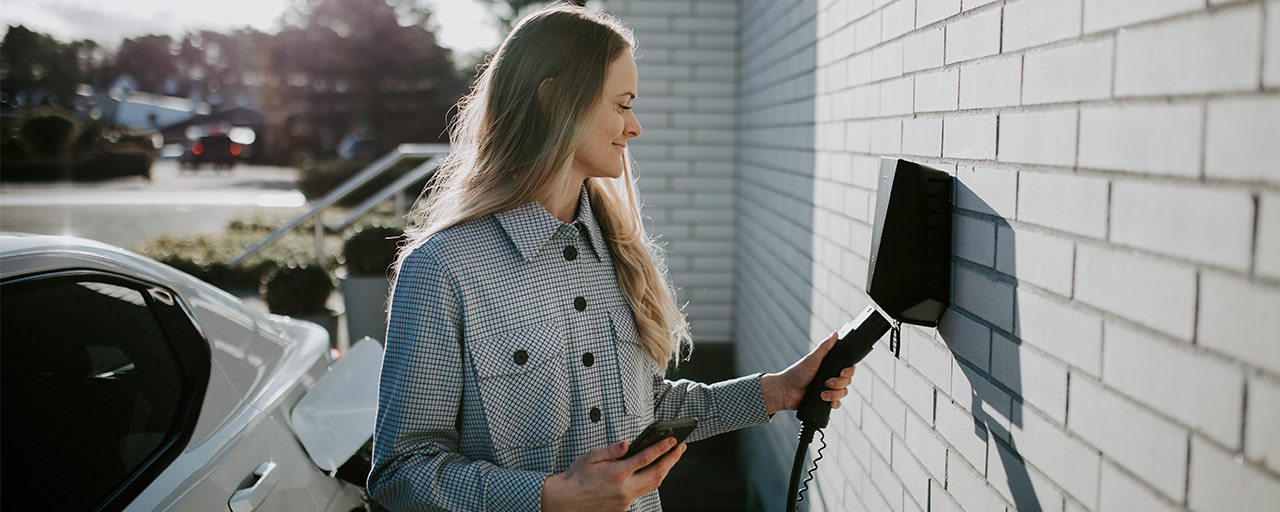 Frau lädt schliesst den Stecker ihres E-Autos an eine Wand-Ladestation an.