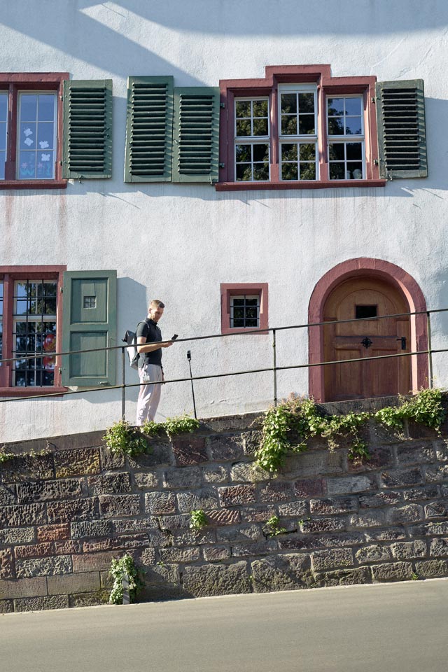 Ein IWB-Mitarbeiter geht vor der Fassade eines historischen Gebäudes mit grünen Fensterläden und roten Fensterrahmen entlang und schaut auf ein Smartphone.
