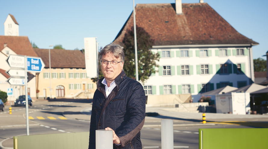 Ein Mann lehnt an ein Geländer. Im Hintergrund sind eine Kirche und Grün zu sehen.