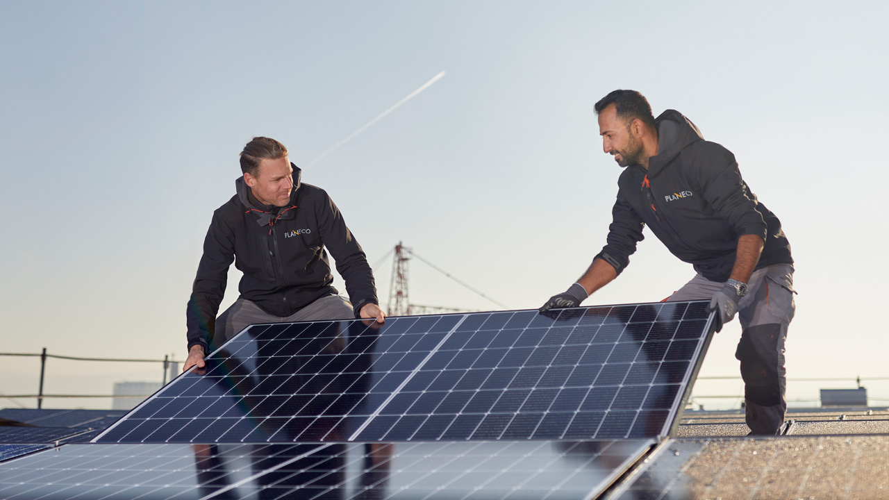 Zwei Männer knien auf einem Flachdach und installieren ein Solarpanel.