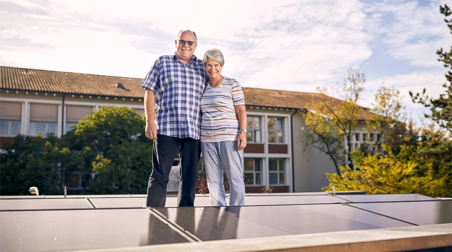 Ein Mann und eine Frau stehen Arm in Arm zwischen Solarpanels auf einem Flachdach.