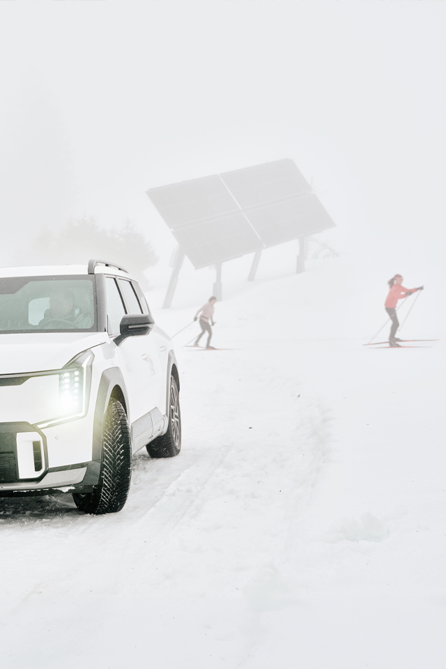 Weisses Elektroauto im Schnee, im Hintergrund eine Solaranlage.  