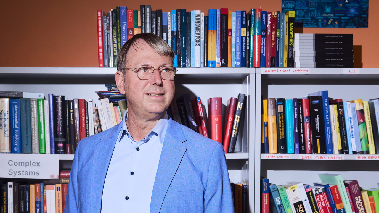 Prof. Dr. Dirk Helbing vor einem Bücherregal mit Büchern in allen Farben.