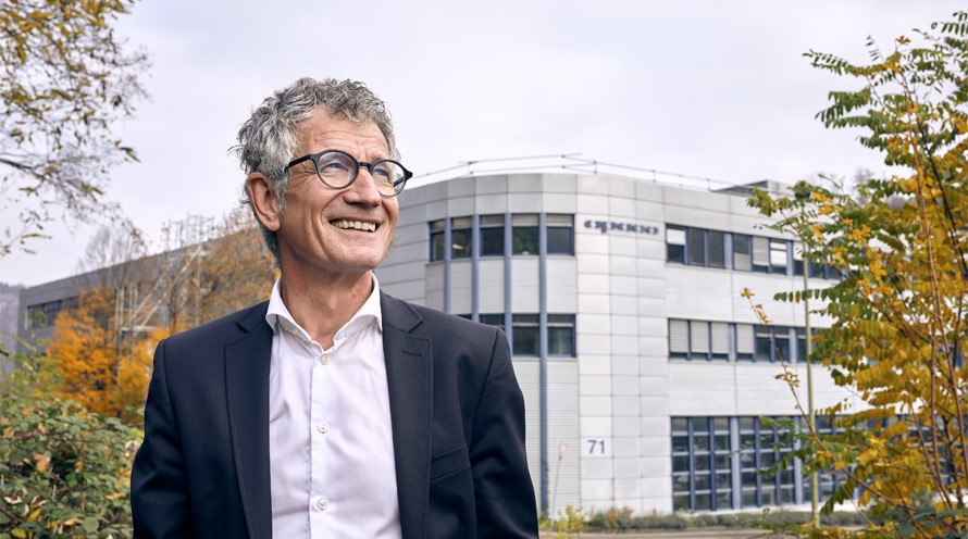 Ein Mann im Anzug steht vor einem mehrstöckigen Industriegebäude und schaut in den Herbsthimmel.