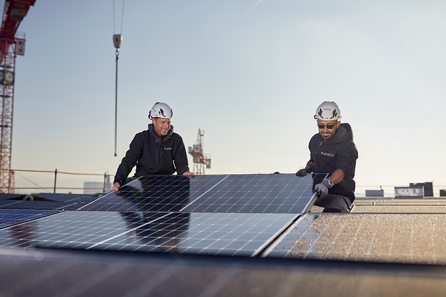 Zwei Männer montieren auf einem Flachdach ein Solarpanel.