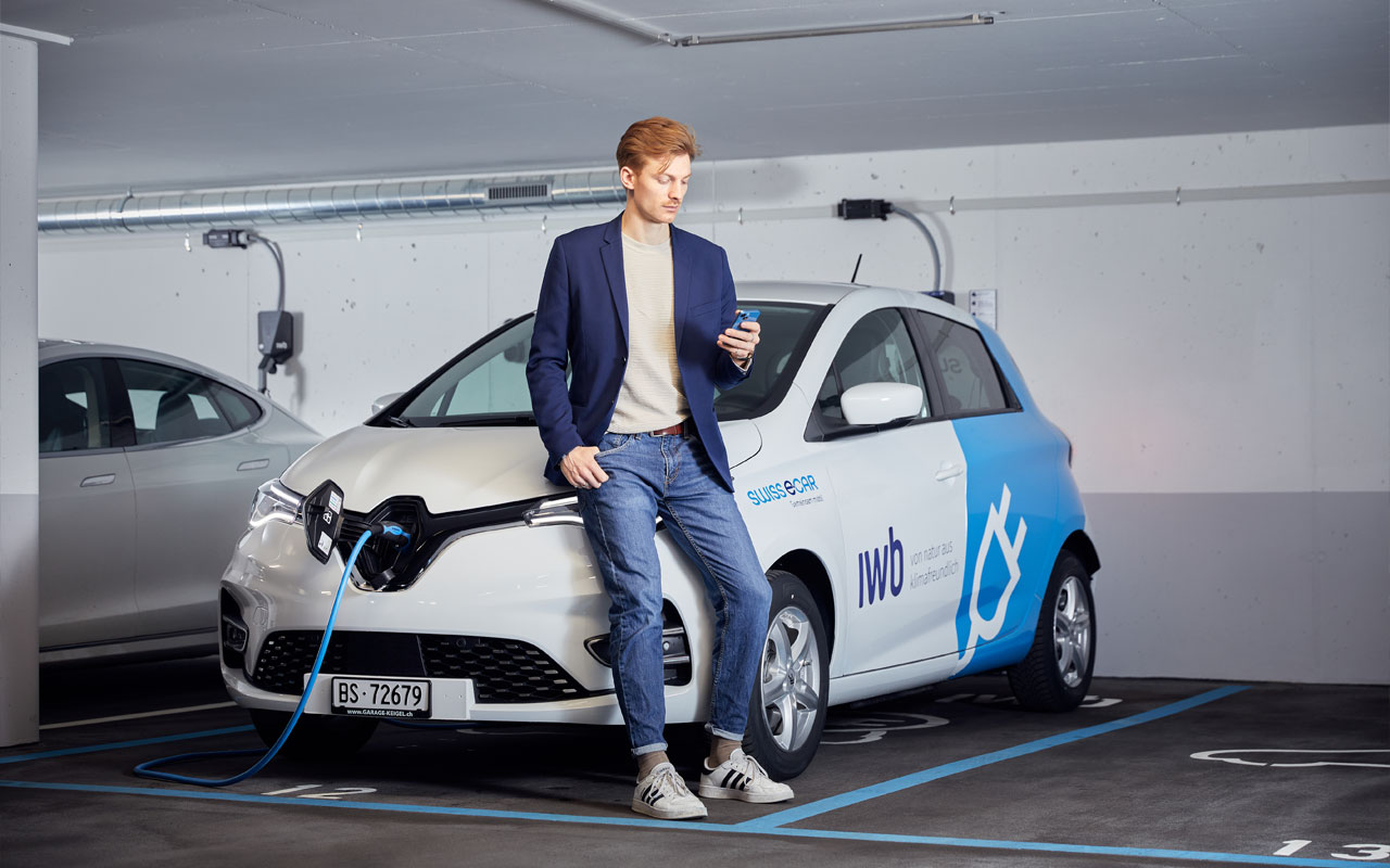 Ein Mann schaut auf sein Handy. Er lehnt sich dabei an ein E-Auto von Swiss E-Car.