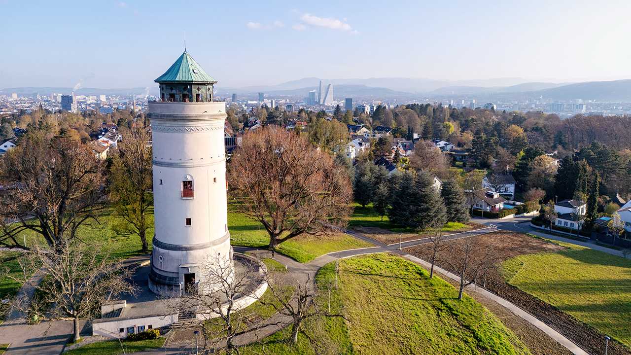 Luftaufnahme des Wasserturms Bruderholz, umgeben von Bäumen und Wiesen. 