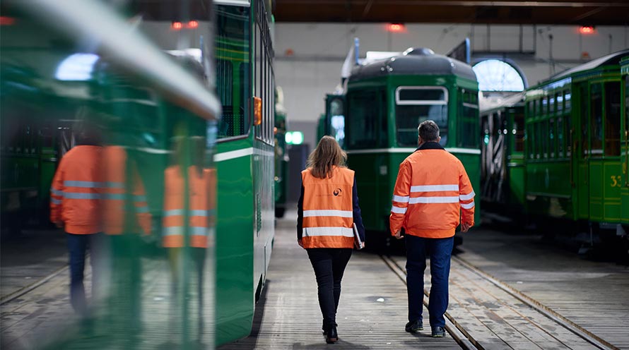 Zwei Personen in orangen Leuchtwesten laufen auf ein stehendes Tram der Basler Verkehrs-Betriebe zu.