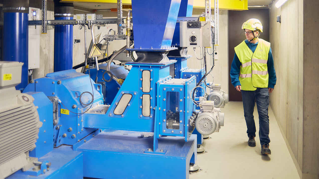 Die Pelletmühle ist himmelblau und kompakt, daneben steht der Projektleiter mit Helm und Leuchtweste.