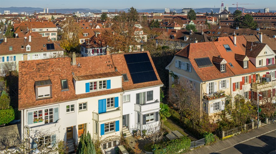 Blick auf mehrere Reihenhäuser. Eines in der Mitte hat eine Photovoltaikanlage auf dem Dach.