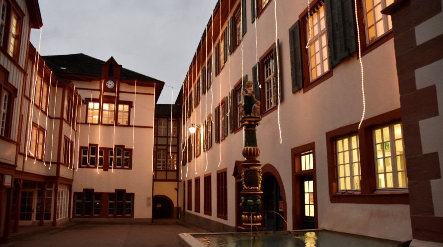 Der Innenhof des Bürgerlichen Waisenhauses Basel. Von den Dächern hängen Lichterketten herunter. Die Licherketten und die Fenster sind erleuchtet.