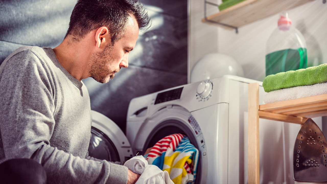 Ein junger Mann steckt Wäsche in eine Waschmaschine.