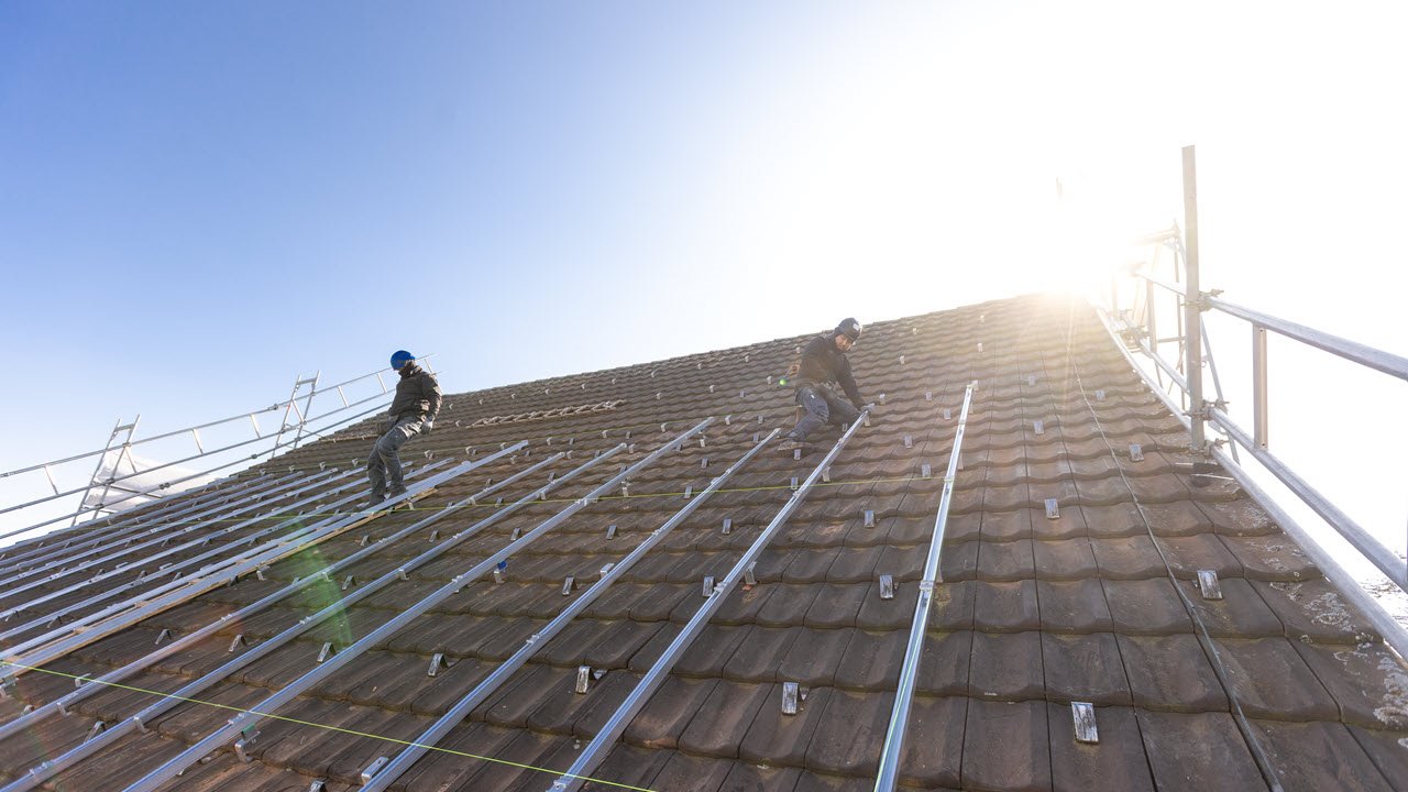 Zwei Senero-MItarbeitende montieren ein PV-Modul auf einem Dach.