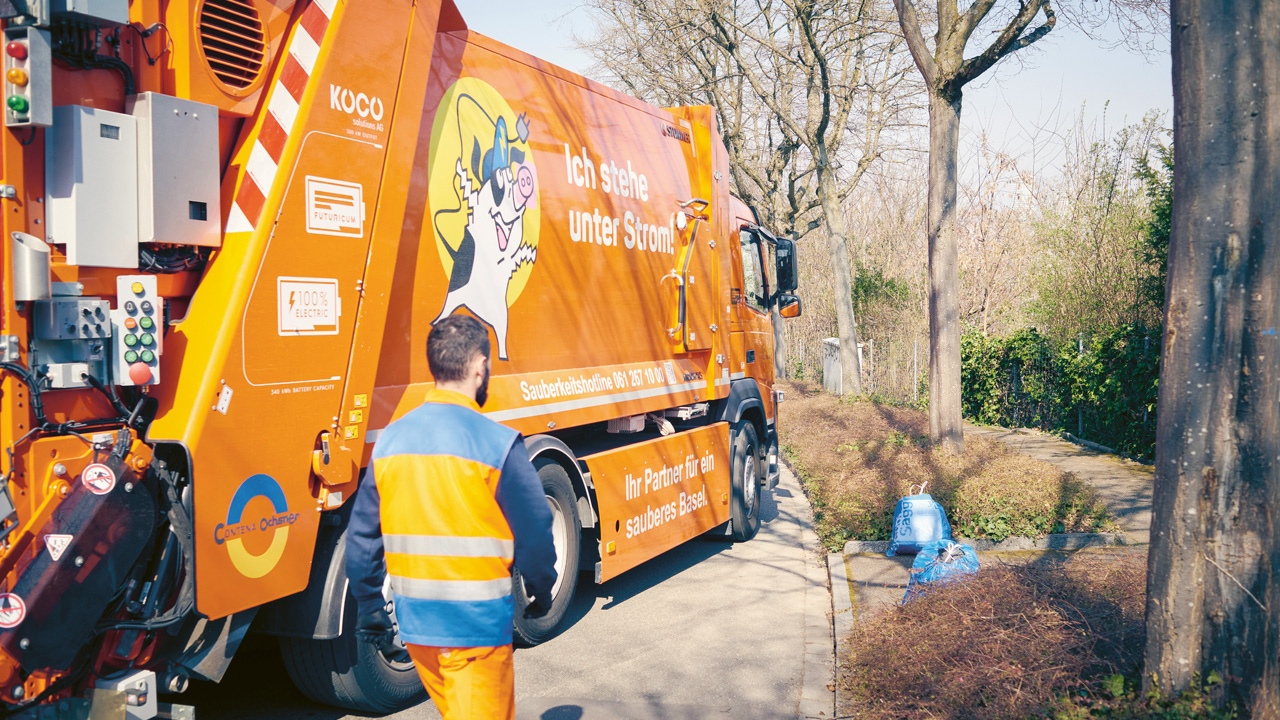 Ein Mann läuft neben einem elektrischen Kehrichtlastwagen, um einen Kehrichtsack aufzuladen.