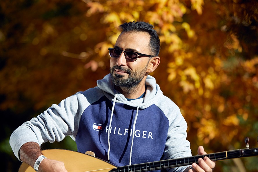 Ein Mann mit Sonnenbrille sitzt im herbstlichen Sonnenlicht und spielt die Saz, ein orientalisches Saiteninstrument.