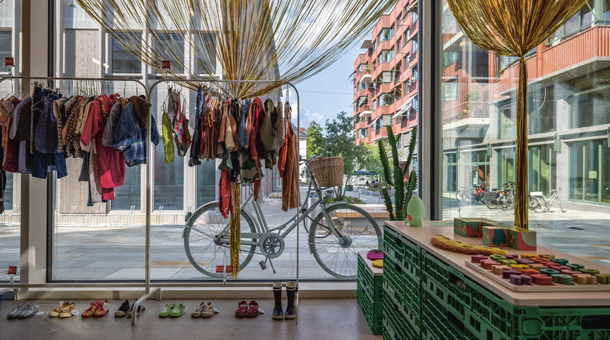 Blick aus dem Secondhandladen in den Innenhof. Vor der grossen Fensterfront des Ladens ist ein Ständer mit Kinderkleidern.