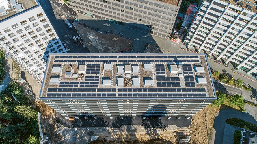 Blick von oben auf das Dach eines Hochhauses, auf dem eine Solaranlage installiert ist.