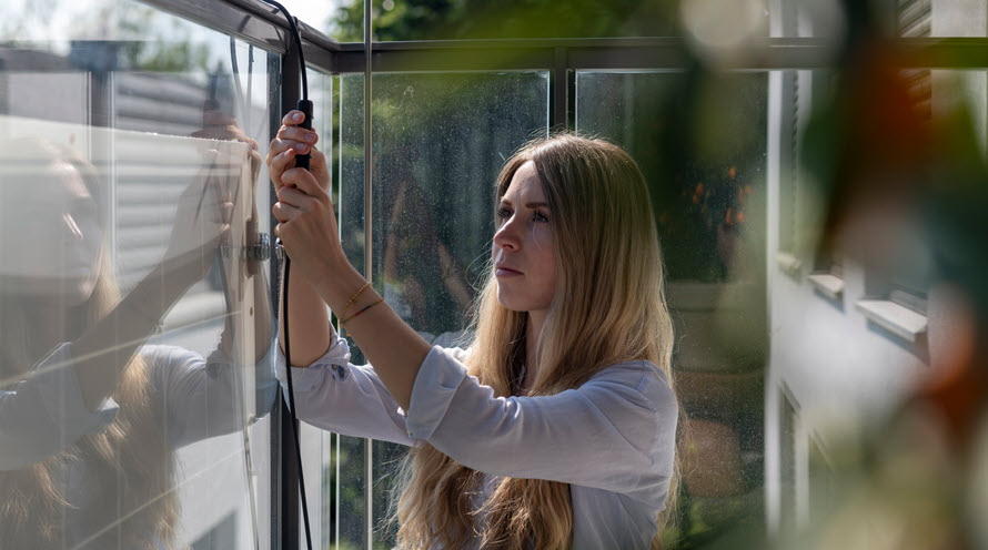 Anna Di Matteo kniet neben dem Balkongeländer und montiert das Kabel ihrer Balkonsolaranlage.
