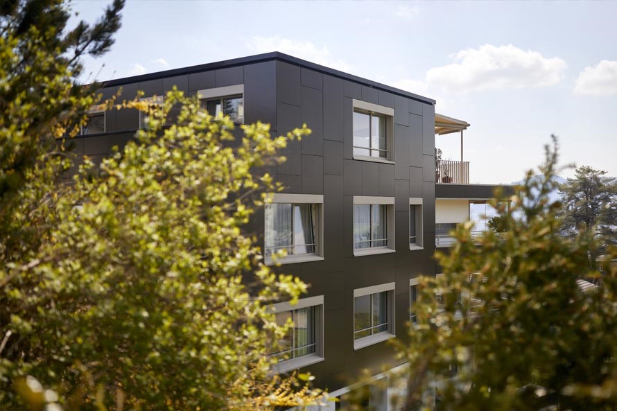 Blick durch Gebüsche auf ein modernes Wohnhaus. Die Fassaden besteht aus Solarpanels.