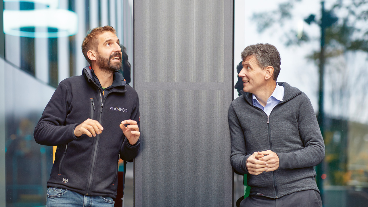 Zwei Männer lehnen an die Wand eines modernen Gebäudes: links Claudius Bösiger, Geschäftsleiter und Mitgründer Planeco, rechts Claus Schmidt, CEO IWB