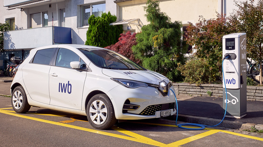 Ein weisses Elektroauto steht neben einer Ladesäule am Strassenrand.