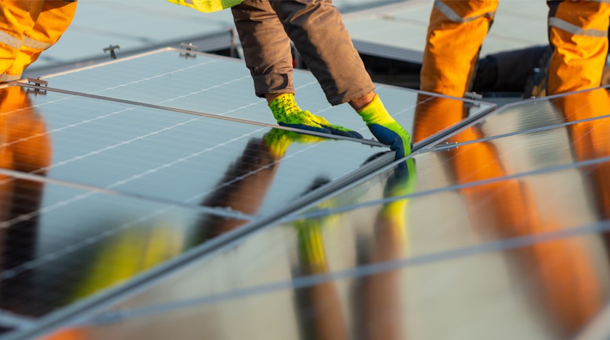 Eine Nahaufnahme von Händen, die auf einem Flachdach ein Solarpanel installieren.